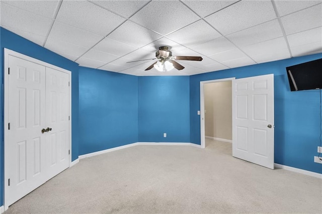 unfurnished bedroom featuring carpet floors, a closet, a ceiling fan, a drop ceiling, and baseboards