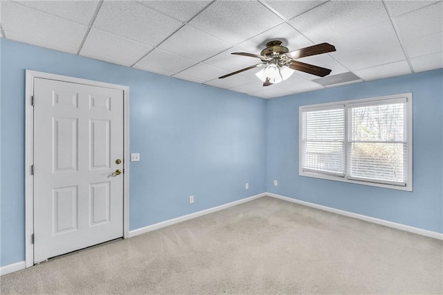 carpeted empty room featuring ceiling fan, baseboards, and a drop ceiling