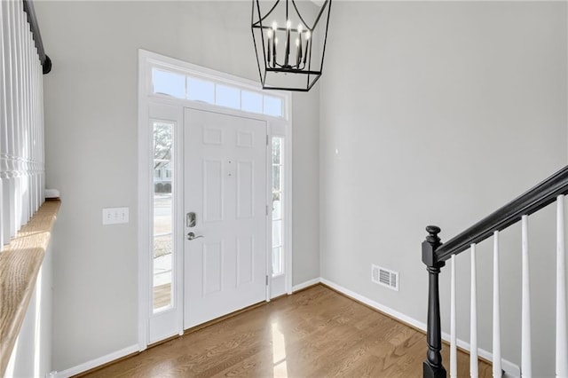 entryway featuring baseboards, visible vents, wood finished floors, an inviting chandelier, and stairs