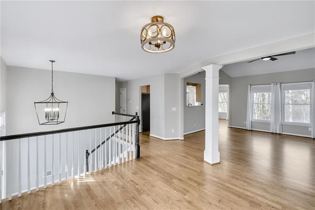 empty room with baseboards, visible vents, an inviting chandelier, wood finished floors, and ornate columns