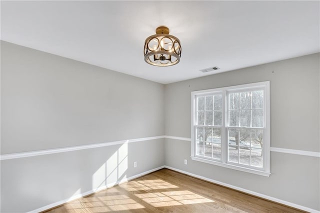 unfurnished room featuring a chandelier, wood finished floors, visible vents, and baseboards