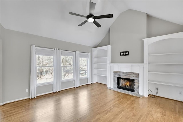 unfurnished living room featuring a warm lit fireplace, ceiling fan, baseboards, and wood finished floors