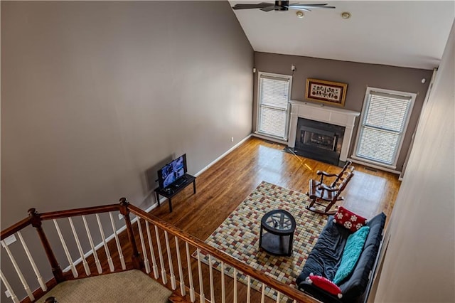 living area featuring lofted ceiling, a fireplace with flush hearth, ceiling fan, wood finished floors, and stairs