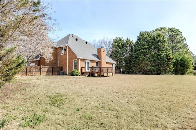 back of property featuring brick siding, a yard, a chimney, fence, and a deck