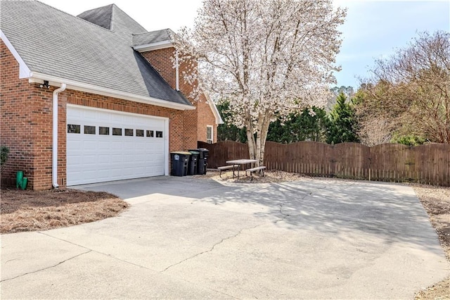 view of side of property with brick siding, roof with shingles, an attached garage, fence, and driveway