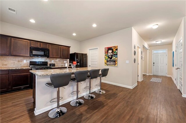 3720 Liverpool Way, Atlanta, GA 30331 - kitchen with a breakfast bar area, light stone counters, black appliances, a center island with sink, and decorative backsplash