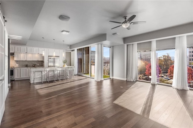 unfurnished living room with dark hardwood / wood-style floors, ceiling fan, and a healthy amount of sunlight