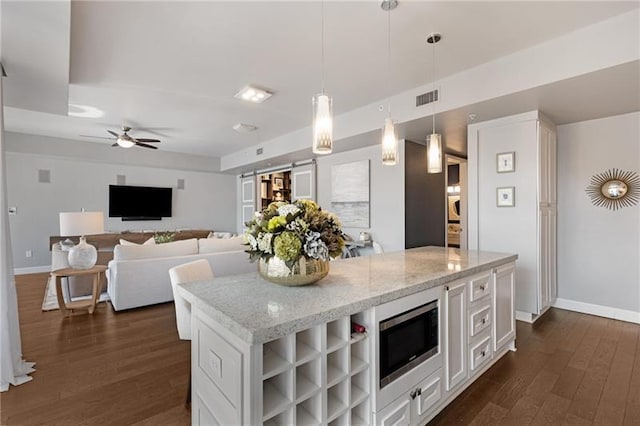 kitchen with light stone countertops, pendant lighting, white cabinets, dark hardwood / wood-style floors, and stainless steel microwave