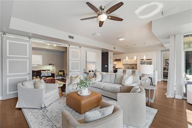 living room with a barn door, ceiling fan, and dark wood-type flooring