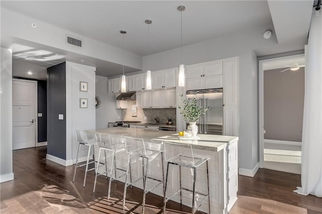 kitchen featuring white cabinets, pendant lighting, a kitchen bar, and built in fridge