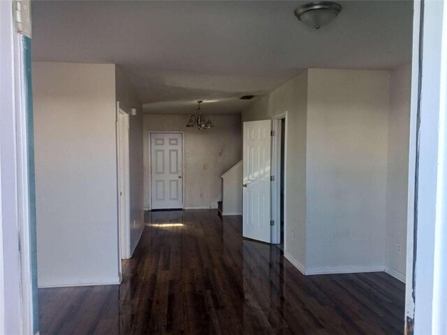 corridor with dark hardwood / wood-style floors and an inviting chandelier