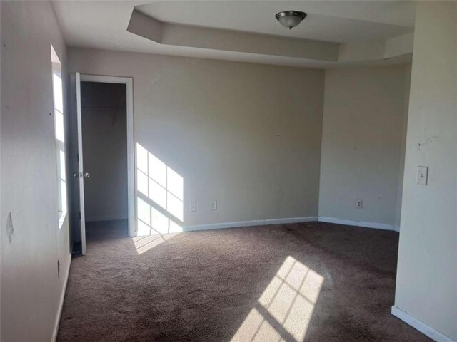 spare room with a tray ceiling and dark carpet