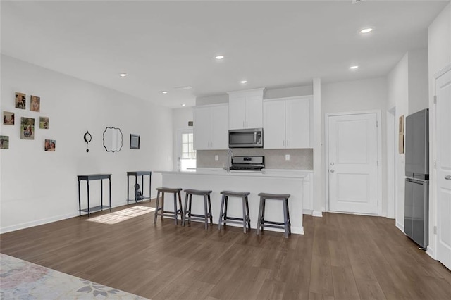 kitchen featuring dark hardwood / wood-style floors, an island with sink, a kitchen breakfast bar, stainless steel appliances, and white cabinets