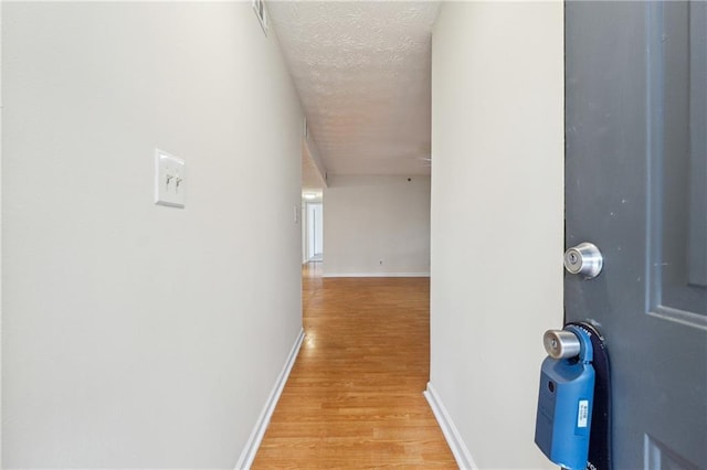 hall with light wood-type flooring, a textured ceiling, and baseboards