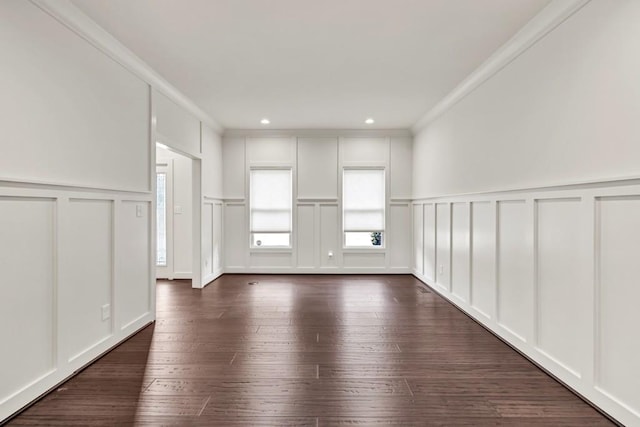 spare room featuring crown molding, a decorative wall, and dark wood-style flooring