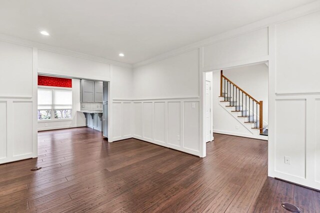 unfurnished room with stairs, crown molding, a decorative wall, and dark wood-type flooring