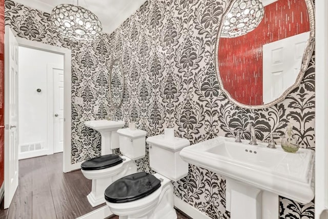 bathroom featuring visible vents, toilet, wood finished floors, wallpapered walls, and a sink