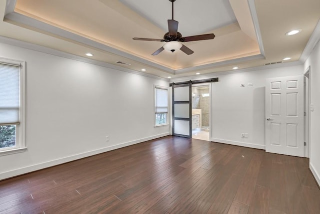 empty room featuring a tray ceiling, dark wood-style flooring, baseboards, a barn door, and visible vents