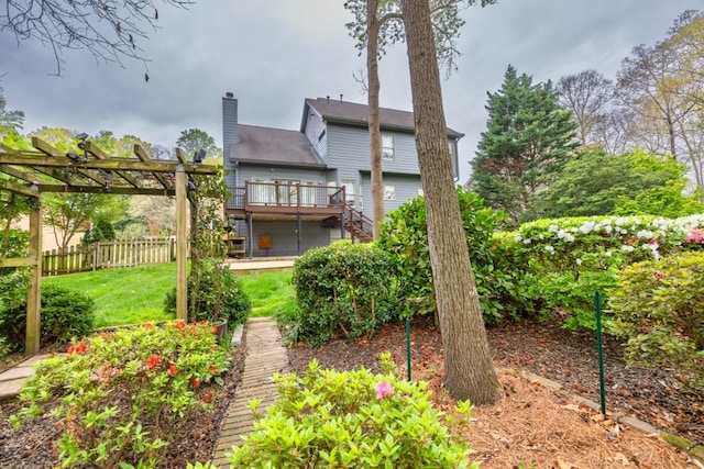 rear view of property featuring fence, a wooden deck, a chimney, a lawn, and a pergola
