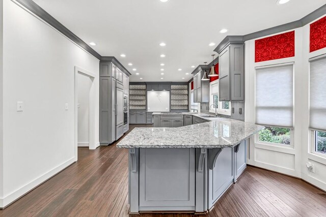 kitchen with a kitchen bar, a sink, light stone counters, gray cabinets, and backsplash