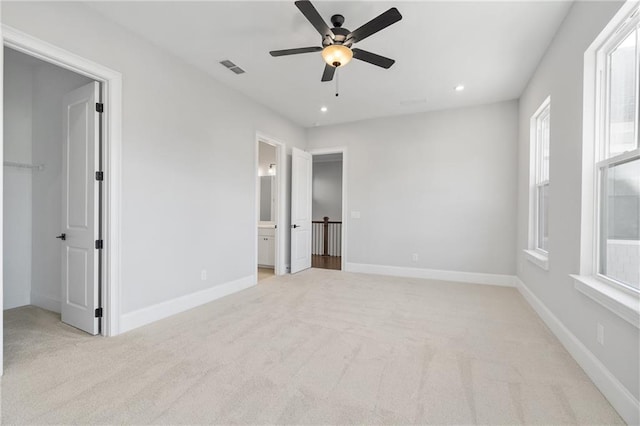 unfurnished bedroom featuring recessed lighting, light colored carpet, visible vents, baseboards, and a walk in closet