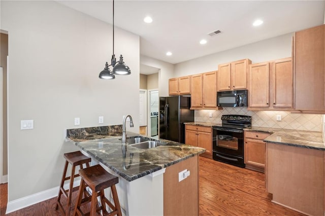 kitchen with pendant lighting, black appliances, sink, dark stone countertops, and light wood-type flooring