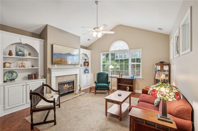 living room featuring built in shelves, ceiling fan, wood-type flooring, lofted ceiling, and a tiled fireplace