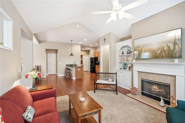 living room with sink, vaulted ceiling, ceiling fan, a fireplace, and wood-type flooring