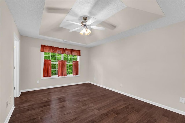 empty room with a raised ceiling, a ceiling fan, dark wood-style flooring, and baseboards