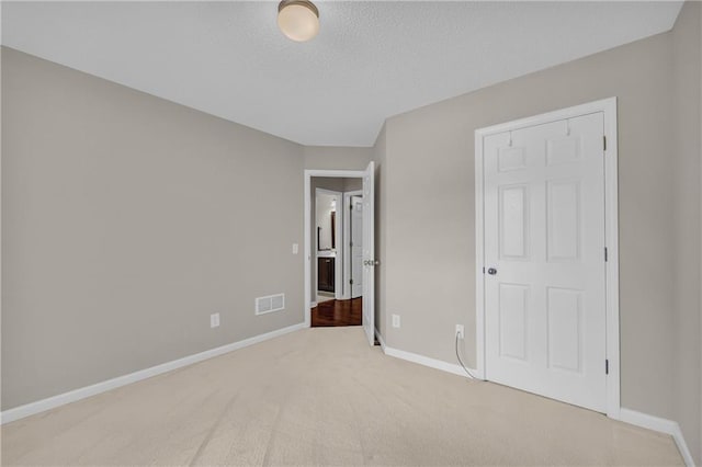 unfurnished bedroom featuring light colored carpet, baseboards, and a textured ceiling