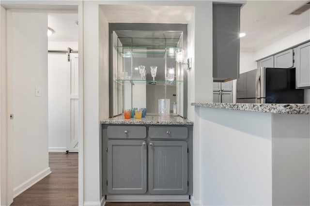 kitchen featuring gray cabinets, stainless steel fridge, dark hardwood / wood-style flooring, and light stone counters