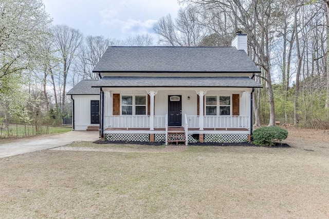 view of front facade featuring a front yard, covered porch, a chimney, a shingled roof, and concrete driveway