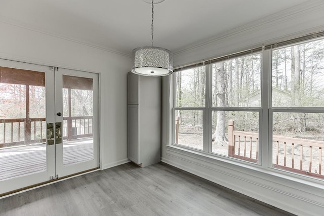 unfurnished dining area with french doors, ornamental molding, and light wood finished floors