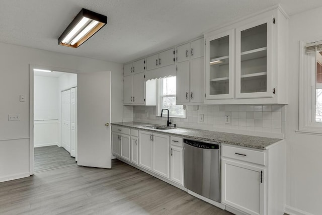 kitchen with tasteful backsplash, light wood-type flooring, stainless steel dishwasher, white cabinetry, and a sink