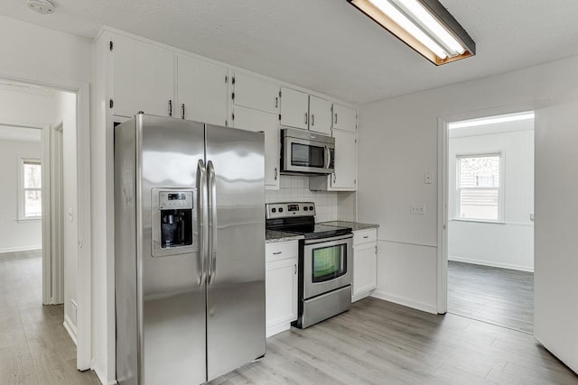 kitchen with tasteful backsplash, appliances with stainless steel finishes, light wood-style flooring, and white cabinets