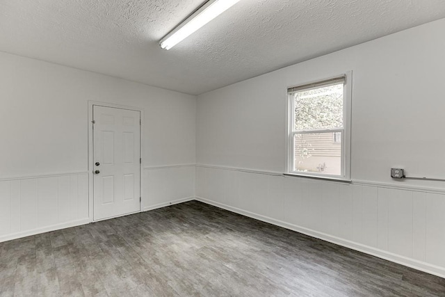 empty room with wood finished floors, a wainscoted wall, and a textured ceiling