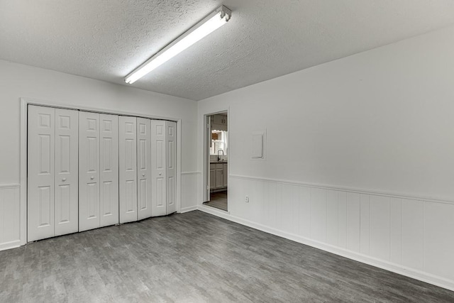 unfurnished bedroom featuring a wainscoted wall, a sink, a textured ceiling, wood finished floors, and a closet