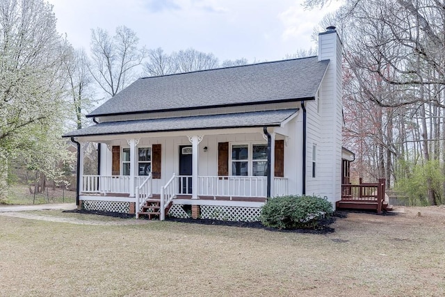 view of front facade with a front yard, covered porch, a chimney, and a shingled roof