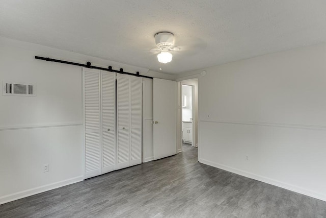 unfurnished bedroom featuring wood finished floors, baseboards, visible vents, a textured ceiling, and a barn door