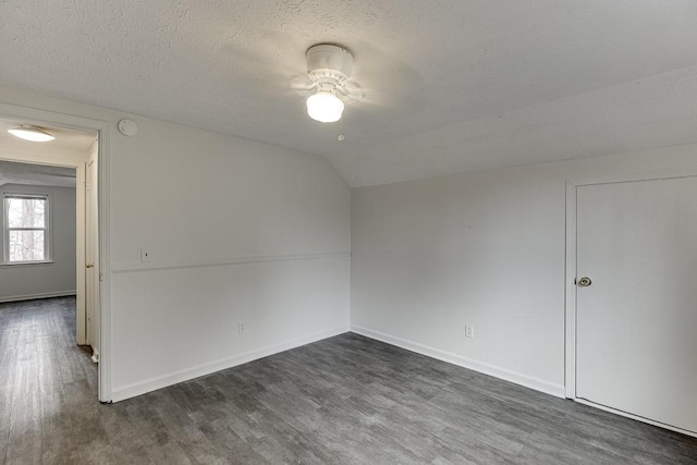 empty room with baseboards, lofted ceiling, dark wood-style flooring, ceiling fan, and a textured ceiling