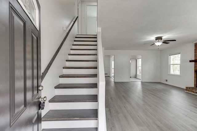 stairs with a textured ceiling, wood finished floors, a fireplace, baseboards, and ceiling fan