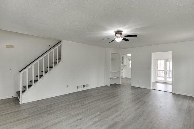 unfurnished living room featuring visible vents, ceiling fan, stairs, wood finished floors, and a textured ceiling