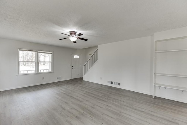 unfurnished living room featuring stairway, wood finished floors, visible vents, ceiling fan, and a textured ceiling