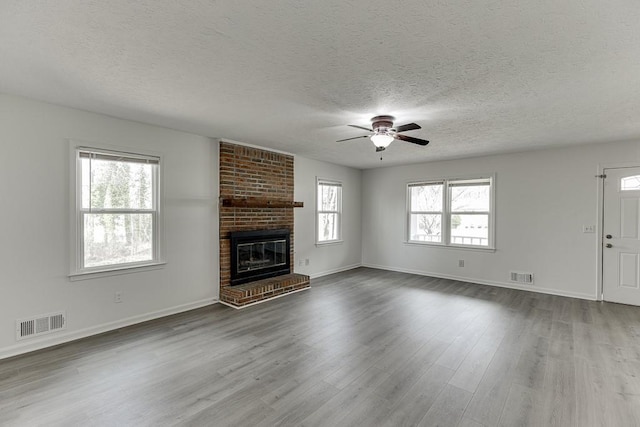 unfurnished living room with ceiling fan, visible vents, dark wood-style floors, and a fireplace