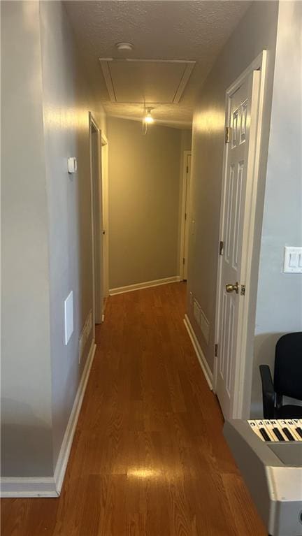 hall featuring attic access, wood finished floors, a textured ceiling, and baseboards
