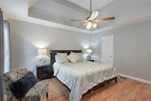 bedroom with a tray ceiling, wood finished floors, baseboards, and ceiling fan