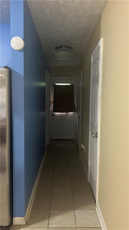 hallway featuring a textured ceiling, light tile patterned flooring, and baseboards