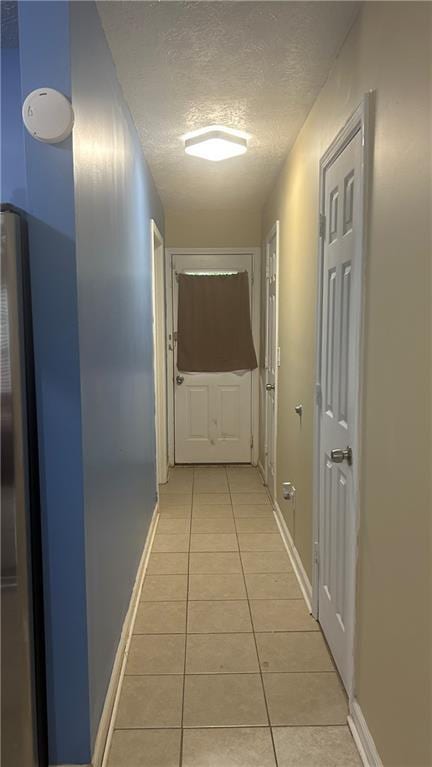 hallway featuring light tile patterned floors, baseboards, and a textured ceiling