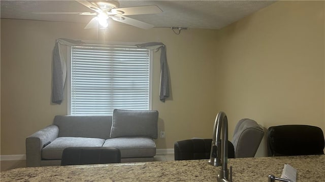 living room with tile patterned flooring, a ceiling fan, baseboards, and a textured ceiling
