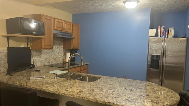 kitchen featuring stainless steel fridge, under cabinet range hood, black electric stovetop, tasteful backsplash, and a textured ceiling
